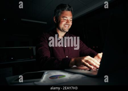 Porträt des erfolgreichen mittleren Alters Geschäftsmann arbeiten Überstunden in seinem Dunkles Büro mit Laptop Stockfoto