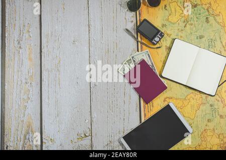 Draufsicht Reiseaccessoires. Sonnenbrille, Reisepass und Devisen, Fotokamera, Notizbuch, Tablet und Weltkarte. Kopierraum. Reisen Stockfoto