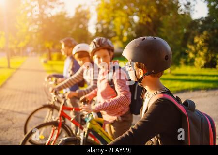 Kinder mit Rucksäcken reiten auf dem Fahrrad im Park in der Nähe der Schule Stockfoto