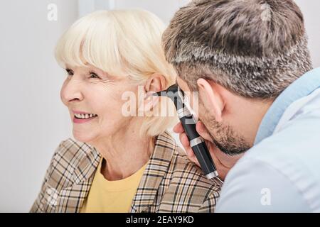 Ältere Frau während der Ohruntersuchung in einer Hörklinik. Audiologe, der das Ohr älterer Patienten mit einem Otoskop untersucht Stockfoto