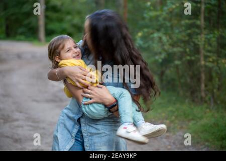 Junge Frau spielt mit Kleinkind Mädchen in gelb im Park. Stockfoto
