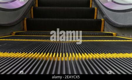 Blick auf die moderne Rolltreppe mit Looped-Perspektive. Automatisierter Aufzugsmechanismus. Gelbe Linie auf Treppe mit violettem Licht beleuchtet. Fut Stockfoto
