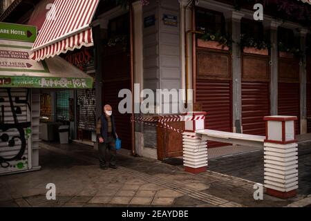 Athen, Griechenland. Februar 2021, 11th. Ein Mann mit einer Mundnase, der die Geschäfte einer Marktstraße bedeckt, läuft entlang. Seit Donnerstagmorgen ist der Großraum Athen erneut einer harten Sperre ausgesetzt, um die Corona-Pandemie einzudämmen, wobei die Polizei die Einhaltung zahlreicher Straßensperren durchgesetzt hat. Quelle: Angelos Tzortzinis/DPA/Alamy Live News Stockfoto