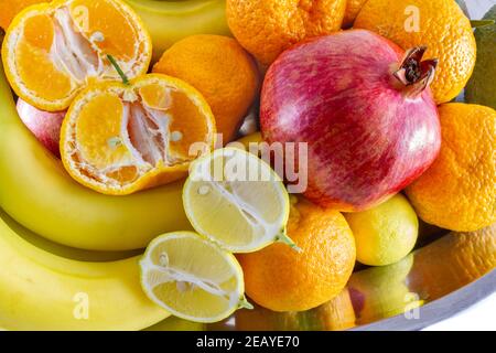 Verschiedene frische Früchte Anordnung von Bananen, Granatapfel, in Scheiben geschnittene Zitrone und in Scheiben geschnittene Mandarine. Stockfoto