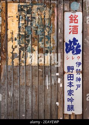 tokio, japan - januar 26 2021: Zerrissene alte japanische Vintage-Plakate des klassischen Films mit einem verrosteten Werbe-Emaille-Zeichen von Reiswein auf dem Corrugate Stockfoto