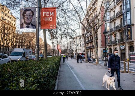 Barcelona, Spanien. Februar 2021, 10th. Ein Mann, der mit seinem Hund läuft, kommt an einem Wahlplakat des sozialistischen Kandidaten Salvador Illa in Barcelona vorbei.der Wahlkampf für die Wahlen zur Regierung Kataloniens der 14F erreicht seine letzten Tage mit einer eher knappen Präsenz von Wahlplakaten im öffentlichen Raum. Kredit: SOPA Images Limited/Alamy Live Nachrichten Stockfoto