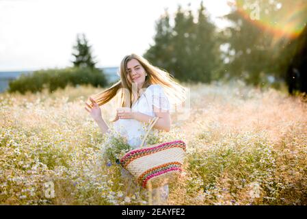 Mädchen auf einem Feld in der untergehenden Sonne mit Gänseblümchen Stockfoto