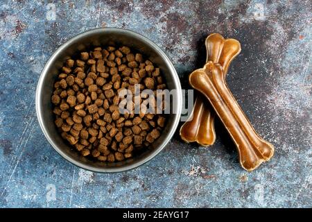 High-Angle-Aufnahme einer Schüssel mit Hundefutter und Kauknochen auf rauer Oberfläche Stockfoto