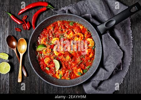 Garnelen Karahi - pakistanische Tomaten-Garnelen-Curry mit Limettensaft Rote Chili und rote Currypaste auf einem Braten serviert Pfanne mit frischem Koriander auf einem dunklen Holz Stockfoto