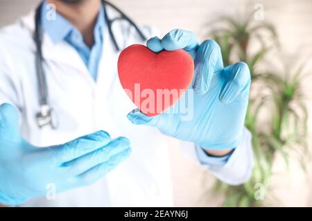 Doktor Hand in Latexhandschuhen hält rotes Herz aus der Nähe Stockfoto
