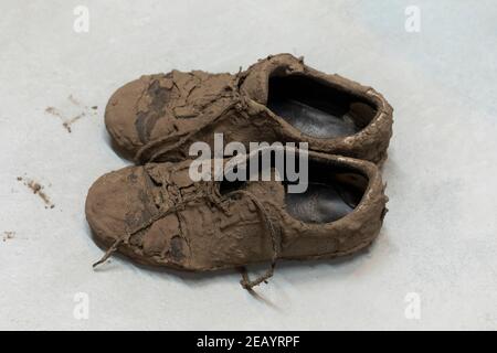Schmutzige, getrocknete schlammige und unordentliche Sneaker-Schuhe, mit denen sie total bedeckt sind Schlamm sah nicht erkennbar aus, während er auf dem Boden lag Stockfoto