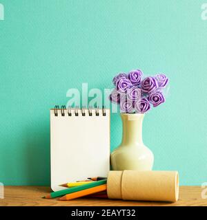 Leeres Notizbuch mit Blumen und Buntstiften auf Holztisch. Grüner Hintergrund Stockfoto