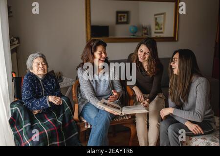 Frauen Generation mit alten kranken Großmutter sitzt im Rollstuhl neben Tochter und Enkelinnen auf der Suche nach einem Fotoalbum. Familie, Generationen concep Stockfoto