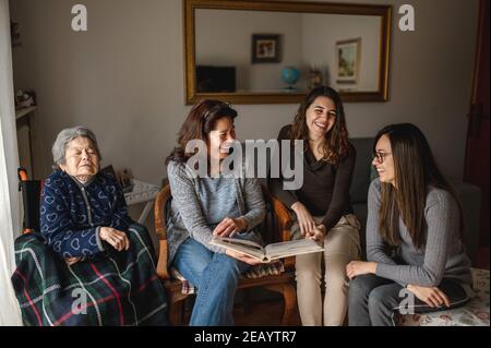 Frauen Generation mit alten kranken Großmutter sitzt im Rollstuhl neben Tochter und Enkelinnen auf der Suche nach einem Fotoalbum. Familie, Generationen concep Stockfoto