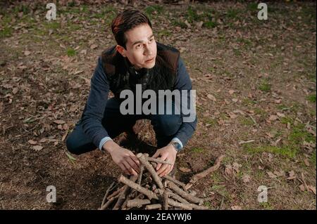 Portrait junger Mann bereitet Holzstapel vor, um Feuer anzuzünden. Camping, natürliches Lifestyle-Konzept. Stockfoto