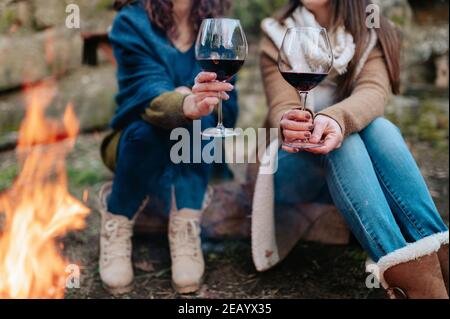 Ein Glas Rotwein aus der Nähe mit nicht erkennbaren Frauen auf dem Hintergrund Neben Lagerfeuer Stockfoto