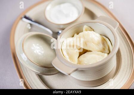Portion ukrainischer russischer Polierknödel gefüllt mit Kartoffel in Ein Keramiktopf mit saurer Sahne serviert Stockfoto