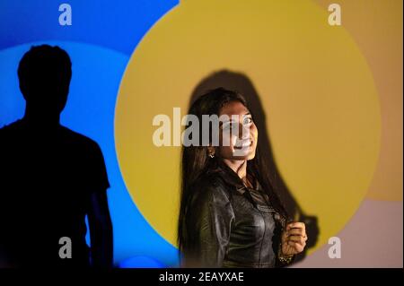Indische Frau mit Leder schwarze Jacke posiert Blick auf die Kamera lächelnd mit Silhouette des schwarzen Mannes. Farbenfroher Hintergrund im Studio beleuchtet von Stockfoto