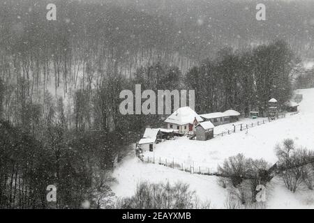 Bauernhaus im Wald während eines schweren Schneesturms, ländliche Szene. Hintergrund mit Schneeflocken für Winterwetter Stockfoto