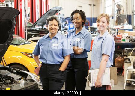 Portrait von drei lächelnden weiblichen Mechanikern in der Autowerkstatt Stockfoto