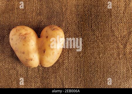 Herzförmige Kartoffel auf rustikalem Leinenhintergrund. Hässliches Essen. Stockfoto