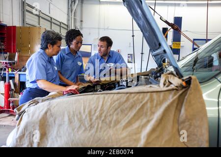 Drei Mechaniker teilen sich ein digitales Tablet und arbeiten an der Planung Ein Auto zur Reparatur Stockfoto