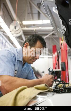 Hispanischer Mechaniker lehnt sich in einen Motor eines Autos er Arbeitet in einer Autowerkstatt Stockfoto