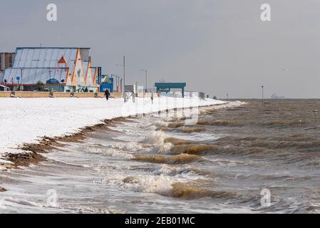 Southend on Sea, Essex, Großbritannien. Februar 2021, 11th. Über Nacht fiel auf Southend weiterer Schnee. Die Leute genießen die Strandpromenade, mit einer Familie am schneebedeckten Strand, während die Wellen gegen die Küste krachen Stockfoto