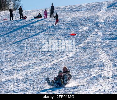 East Lothian, Schottland, Großbritannien, 11th. Februar 2021. UK Wetter: Sonne und Schnee zum Rodeln. Kinder und Familien haben Spaß Rodeln auf Skid Hill im Winterschnee als Mann und kleiner Junge gehen die Piste auf einem Schlitten Stockfoto