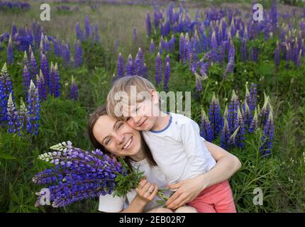 Familienwochenende. Glückliche Mutter und niedlichen Sohn umarmen unter den Wildblumen auf dem Feld. Mütterliches Glück. Ruhe in der Natur. Muttertag Stockfoto