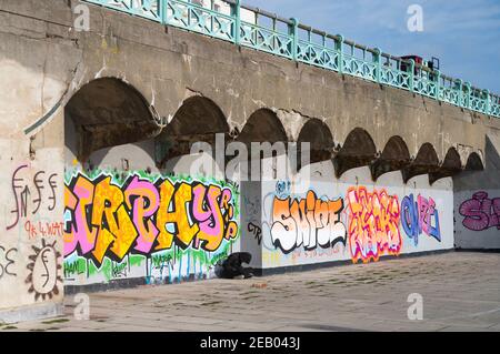 Brighton UK 11th February 2021 - EIN junger Mann sitzt unter einer hellen Graffiti-Kunst an der Küste von Brighton, während die Regierungen die Restriktionen weiter : Credit Simon Dack / Alamy Live News Stockfoto