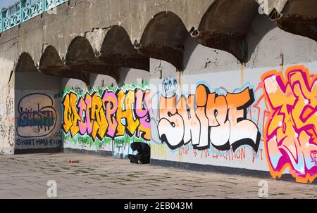 Brighton UK 11th February 2021 - EIN junger Mann sitzt unter einer hellen Graffiti-Kunst an der Küste von Brighton, während die Regierungen die Restriktionen weiter : Credit Simon Dack / Alamy Live News Stockfoto