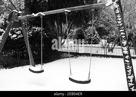 Einsame Schaukeln auf leerstehendem, schneebedecktem Kinderspielplatz. Einsamkeit im Winter. Schwarzweiß-Foto. Stockfoto