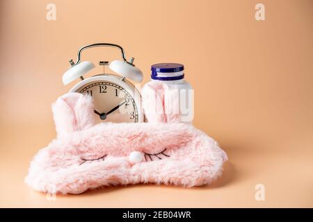 Pills Flasche, Schlafmaske und Wecker auf rosa Pastelltönen Hintergrund. Konzept Schlafstörungen, Schlafstörungen, Zeit, Pillen und Behandlung zu nehmen. Stockfoto