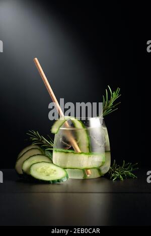 Kaltes Erfrischungsgetränk mit Eis, Gurke und Rosmarin. Das gefrorene Glas auf einem schwarzen Tisch. Stockfoto