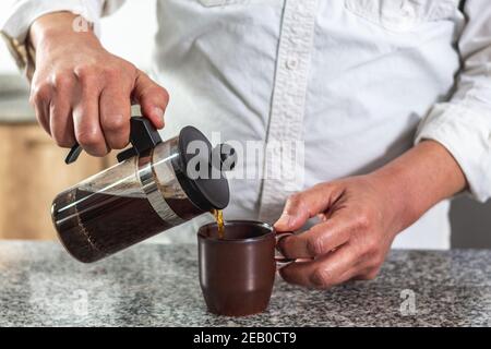 Nahaufnahme der Hände beim Eingießen einer Tasse Kaffee Eine französische Presse Stockfoto