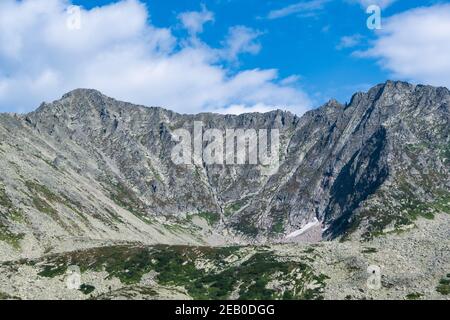 Bergtal mit Steinkamm und Bäumen am Horizont. Reisen Sie im Sommer durch wilde Felsen. Berglandschaft gegen blauen Himmel an sonnigen Tagen Stockfoto