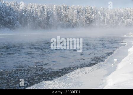 Frostiger Nebel über dem Winterfluss mit Schnee und Wald am Ufer. Erstes Eis am See an kalten Tagen. Stockfoto