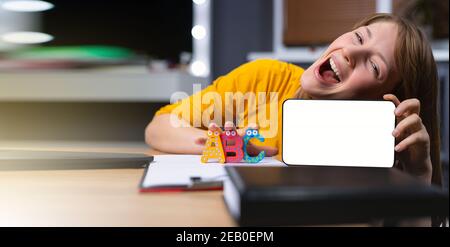 Banner, Langformat. Junge glückliche und energische Englischlehrerin posiert mit Buchstaben und Smartphone. Online-Unterricht und Nebenraum. Stockfoto