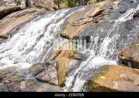 Kleiner Wasserfall, der über einem großen Felsen an einem berühmten Ort in der Nähe eines immergrünen Waldes fließt. Stockfoto