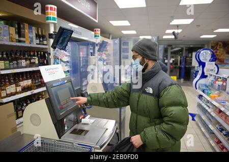 Sheffield, Großbritannien, 14th. Januar 2021: Ein junger Mann mit Gesichtsmaske und Winterkleidung zahlt an einem Tesco Express-Selbstbedienungskassen Lebensmittel Stockfoto