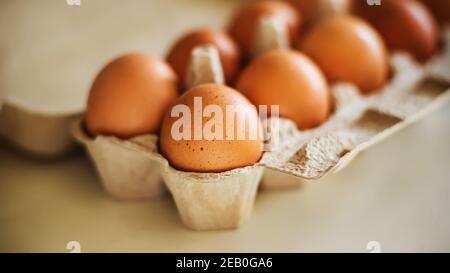 Braune Hühnereier liegen in einer Pappschachtel, sind auf einem weißen Tisch und von Sonnenlicht beleuchtet. Gesundes Essen zum Frühstück. Stockfoto