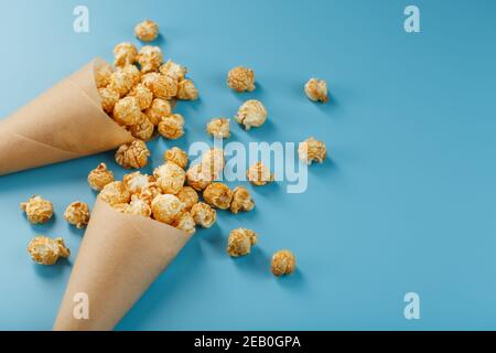 Karamell Popcorn in einem Papierumschlag auf blauem Hintergrund. Köstliches Lob für das Ansehen von Filmen, TV-Serien, Cartoons. Freier Speicherplatz, Nahaufnahme. Minimalisti Stockfoto