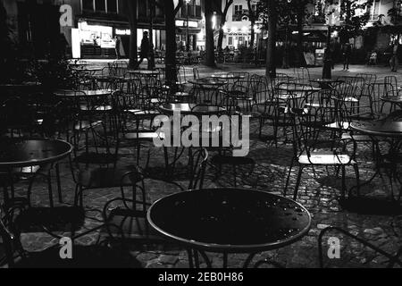 Pariser Nacht Stadtszene nach Regen. Verschwommene Lichter der Bars und Geschäfte spiegeln sich auf leeren nassen Cafeterien und Pflastersteinpflaster. Schwarzweißfoto Stockfoto