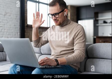 Videoanruf-Konzept. Ein junger Mann verwendet einen Laptop für Video-Verbindung, Remote-Meeting, ein junger Mann winkt hallo, schaut auf die Webcam froh zu sehen Stockfoto