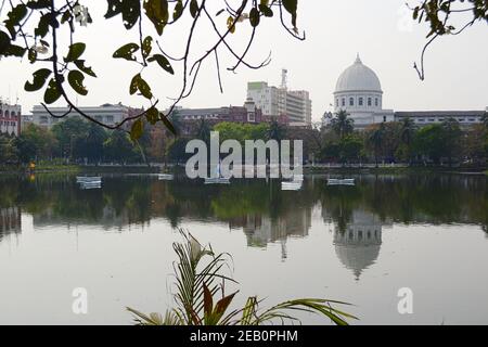 Blick auf den Lal Dighi See oder den Roten Pool mit Booten durch grünes Laub. Das Gebäude der Post spiegelt sich im Wasser wider. Historische Kolonialarchitektur Stockfoto