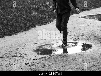 Kindheit Spaß Tage Nostalgie Erinnerungen. Junge in gestreiften Regenstiefeln, die durch Pfützen im Wald wandern. Einfache Lebensfreude, gesunde natürliche Lifestyle-Konzept Stockfoto