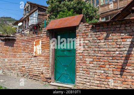 Vintage verwitterte grüne Metalltür unter rostigen Visier in roten Ziegelwand. Alte Tiflis Architektur, Georgien Stockfoto