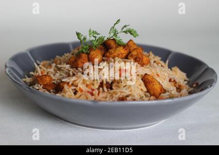 Tomatenreis serviert mit Raita und gebratenen Hähnchenbissen ohne Knochen. Aufnahme auf weißem Hintergrund. Serviert auf einer grauen Schüssel Stockfoto