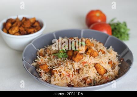 Tomatenreis serviert mit Raita und gebratenen Hähnchenbissen ohne Knochen. Aufnahme auf weißem Hintergrund. Serviert auf einer grauen Schüssel Stockfoto